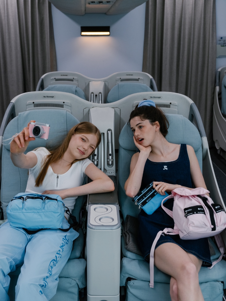 機内の座席で自撮りをする2人の女性とピンクのリュック