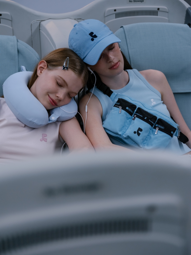 機内でネックピローをして眠る2人の女性と水色のバッグ