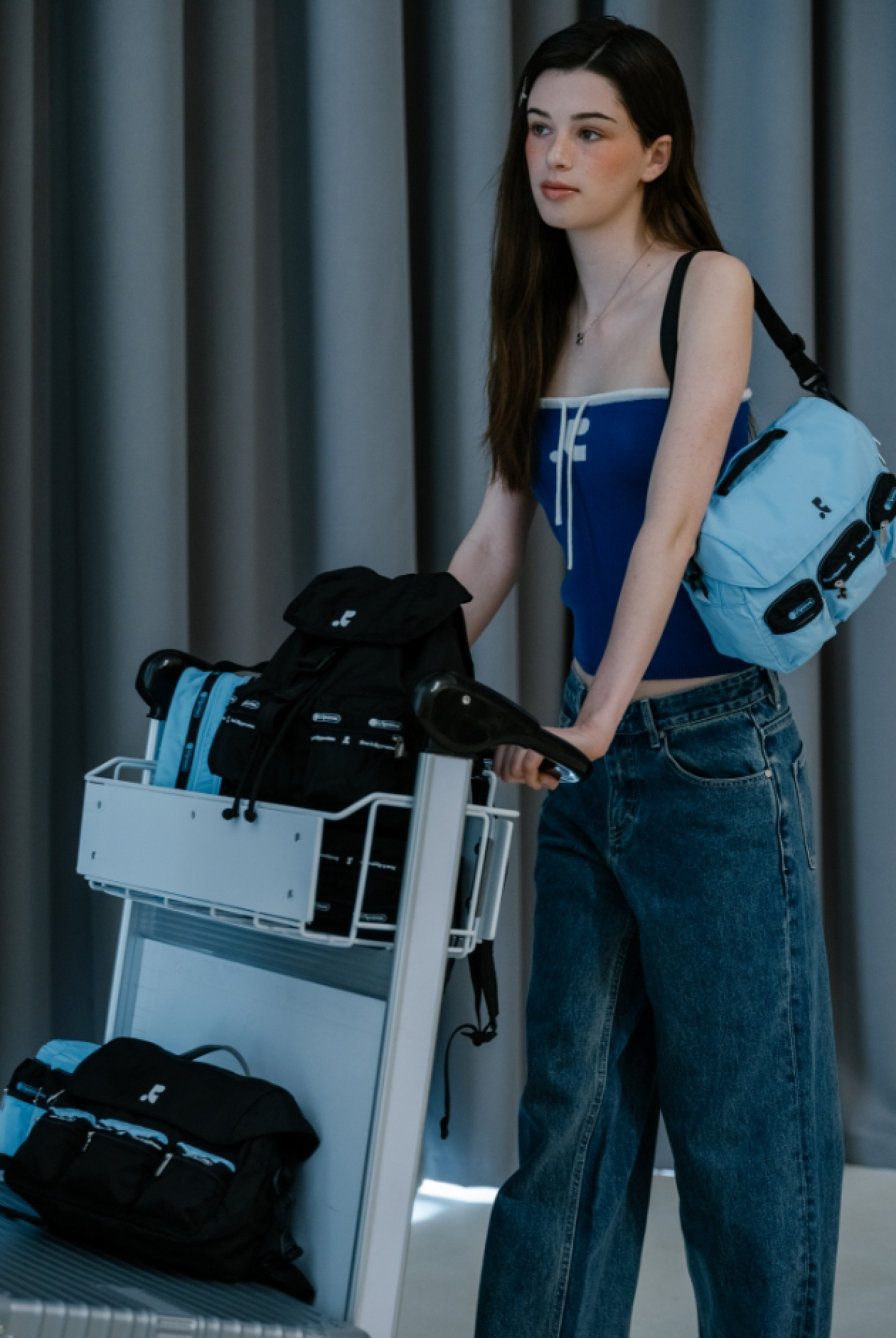 水色のショルダーバッグを掛け、荷物を積んだ空港カートを押す女性