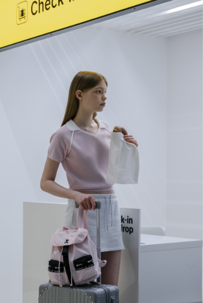 ピンクのリュックをスーツケースに載せて立つ女性