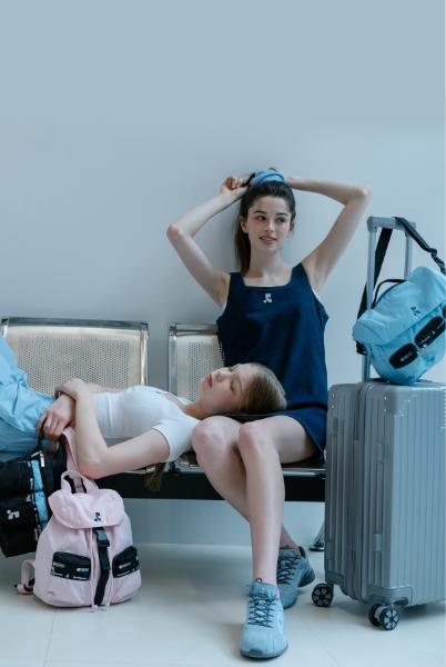 空港のベンチで寝そべる女性と、座って髪を触る女性