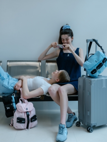 空港のベンチで寝そべる女性をカメラで撮影する女性とスーツケース