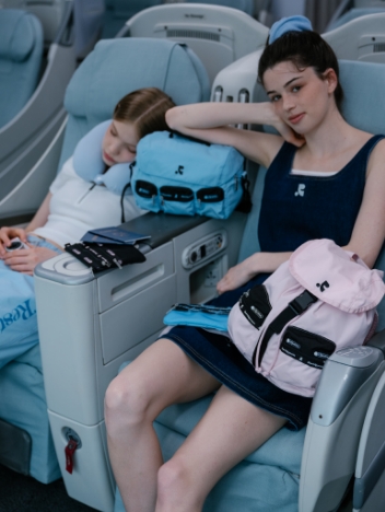 機内の座席でくつろぐ2人の女性と水色とピンクのバッグ